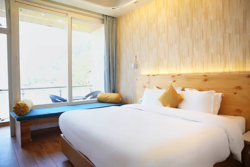 A deluxe room with a cedar feature wall, a wide bed and a cushioned window seat opening onto a balcony.