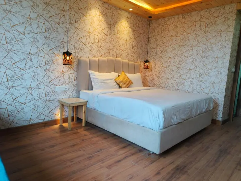 A deluxe room with a king bed, patterned wallpaper, warm pendant lights and a timber ceiling.