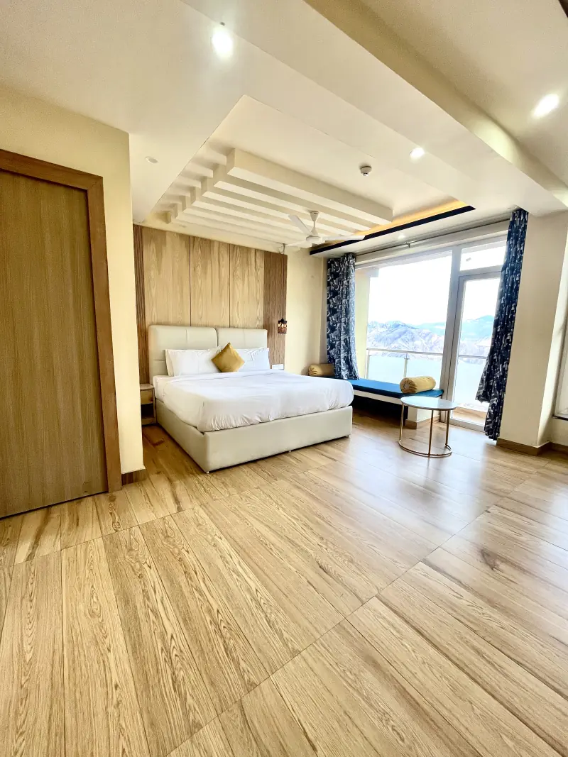 A large bright family room with a king bed and floor-to-ceiling glass opening onto a balcony with a mountain view.