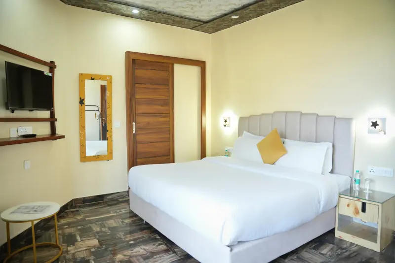 A standard room with a double bed, wall-mounted television, mirror and a wooden wardrobe.