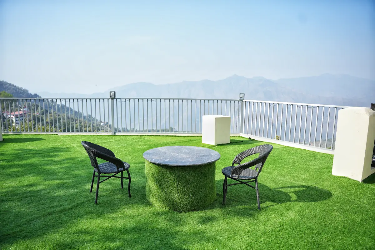 A table and two chairs on the rooftop lawn, with the railing and a long blue mountain ridge behind.